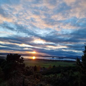 sunset over Loch Leven, with a mottled blue and purple sky and a ball of sun in the water